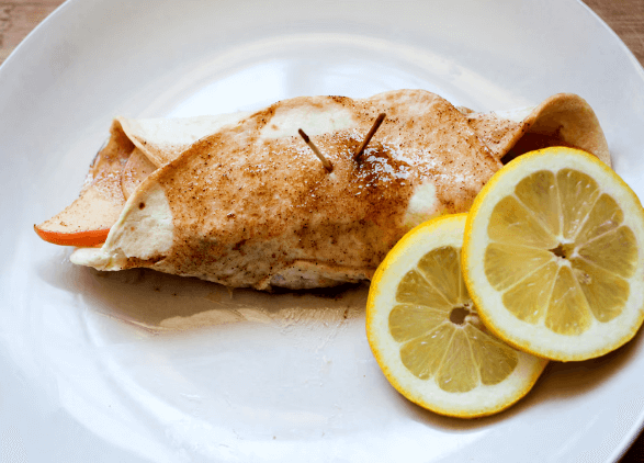 Apple slices in a tortilla with cinnamon on a white plate with two lemons.