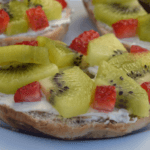 bagel with cream cheese topped with kiwi slices and chopped strawberries.