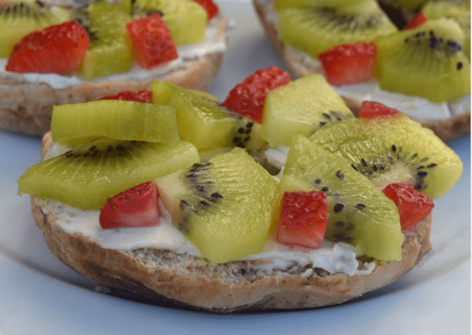 bagel with cream cheese topped with kiwi slices and chopped strawberries.