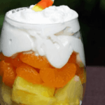 Glass with pineapple chunks, mangrine orange slices, and whipped cream on top.