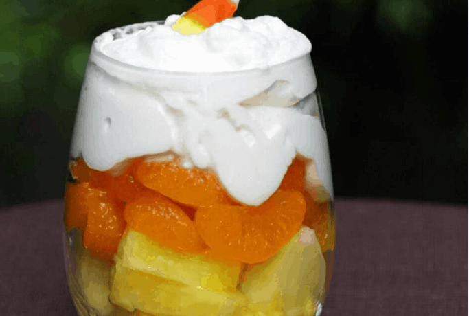 Glass with pineapple chunks, mangrine orange slices, and whipped cream on top.