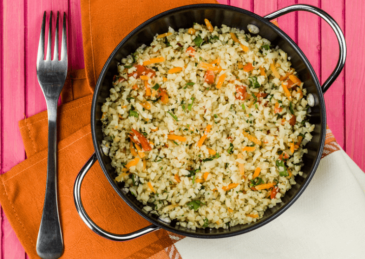 Cauliflower stir fry with chopped vegetables in a pot with a fork next to it.