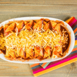 Enchiladas in a white dish with shredded cheese.