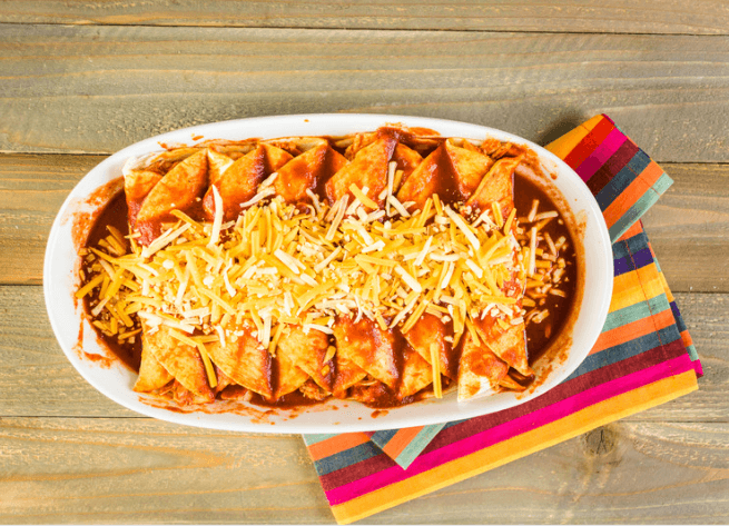 Enchiladas in a white dish with shredded cheese.