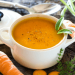 Carrot coconut soup in a white bowl with carrots surrounding it.