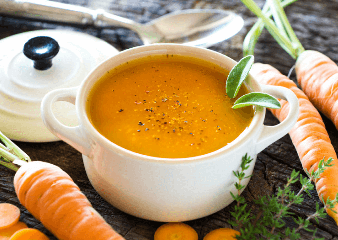 Carrot coconut soup in a white bowl with carrots surrounding it.