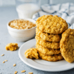 Stack of pumpkin oatmeal cookies on a white plate with a glass of milk and wash cloth in the back.