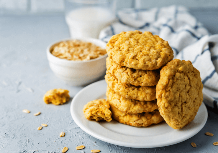Stack of pumpkin oatmeal cookies on a white plate with a glass of milk and wash cloth in the back.