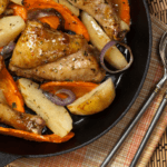 Roasted chicken, carrots, and potatoes in a black skillet.