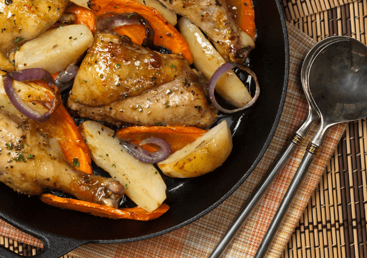 Roasted chicken, carrots, and potatoes in a black skillet.