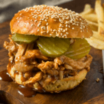 BBQ pulled chicken on a bun with french fries in the back.