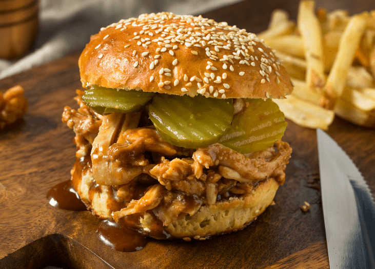 BBQ pulled chicken on a bun with french fries in the back.