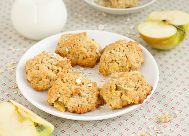 Oatmeal cookies on a white plate with halved apples.