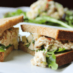 A tuna sandwich with lettuce and bread sliced in half on a white plate.