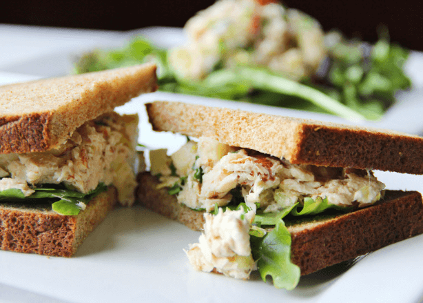 A tuna sandwich with lettuce and bread sliced in half on a white plate.