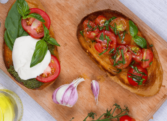 Balsamic dressing, tomatoes, mozzarella, and spinach on two pieces of bread on a wooden cutting board.