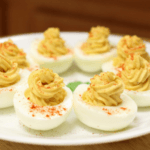 Eight deviled eggs on a white plate, sprinkled with paprika.