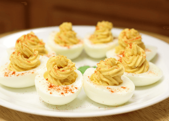 Eight deviled eggs on a white plate, sprinkled with paprika.