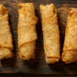 Four eggs rolls on a wood table.