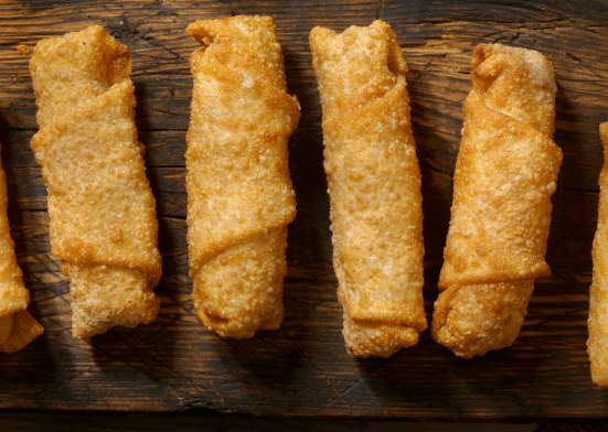 Four eggs rolls on a wood table.