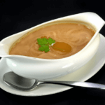 White gravy boat with chicken gravy and fresh herbs and a spoon.