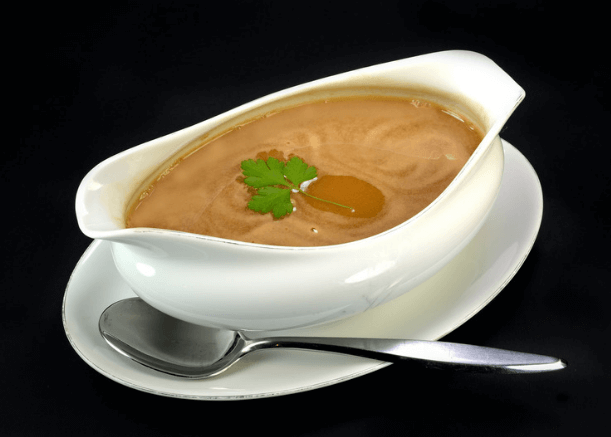 White gravy boat with chicken gravy and fresh herbs and a spoon.