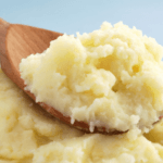 Thick, creamy mashed potatoes with a wooden spoon.