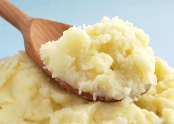 Thick, creamy mashed potatoes with a wooden spoon.