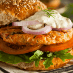 Salmon burger on a bun with lettuce tomato onion and mayo.