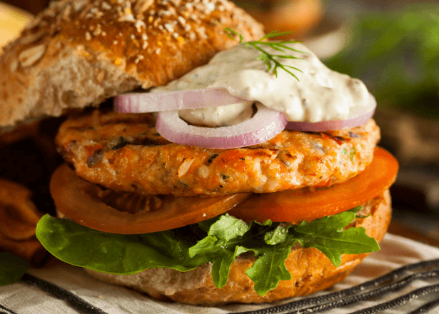 Salmon burger on a bun with lettuce tomato onion and mayo.