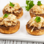 Four cheese stuffed mushrooms on a white plate.