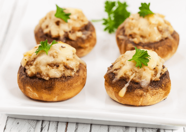 Four cheese stuffed mushrooms on a white plate.