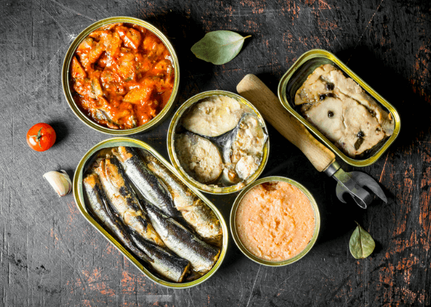 An opened canned tuna, canned sardines, canned mackerel on a black surface.