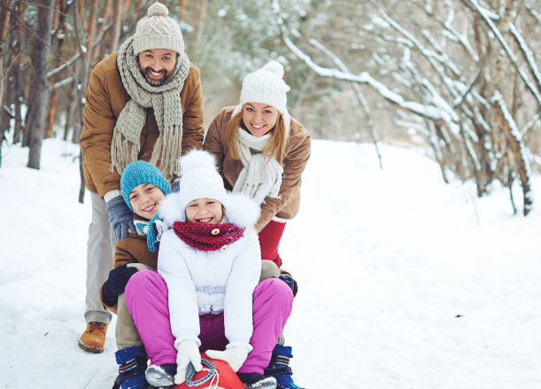 Mom, dad, and two children playing in the snow on a sled.