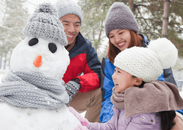 Mom dad, and child smiling looking at a snowman.