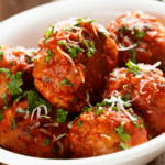 Teriyaki meatballs with herbs in a white bowl.