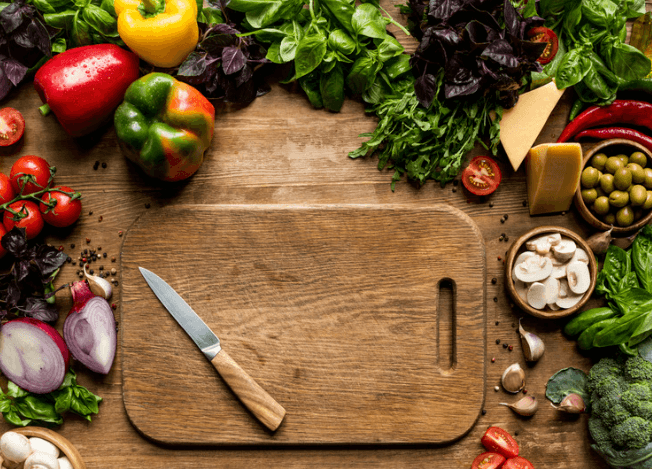 Cutting board with a knife and assorted vegetables around it.