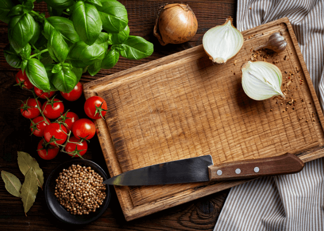 cutting board with knife, onion, tomatoes, and greens.