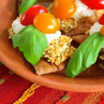 Eggplant in breadcrumbs with tomatoes and basil on top.