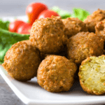 Stacked falafel balls with lettuce and tomatoes.