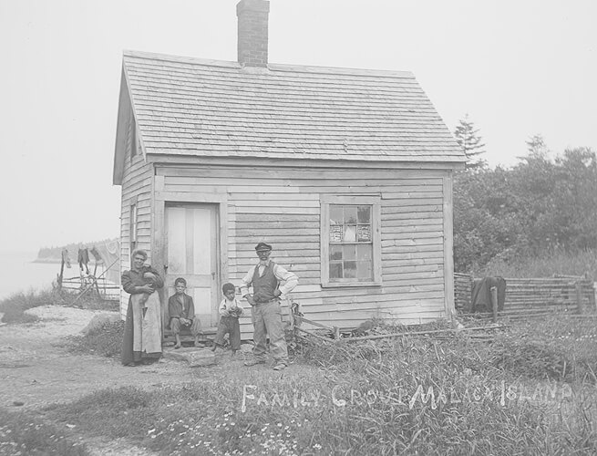 An antique photo of a family posing in front of a house.