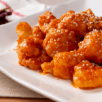 Orange shrimp with sesame seeds on a white plate.