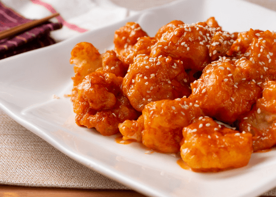 Orange shrimp with sesame seeds on a white plate.