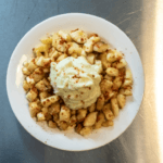 Yuca fries in a white bowl with dip on top.