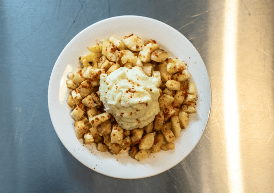 Yuca fries in a white bowl with dip on top.