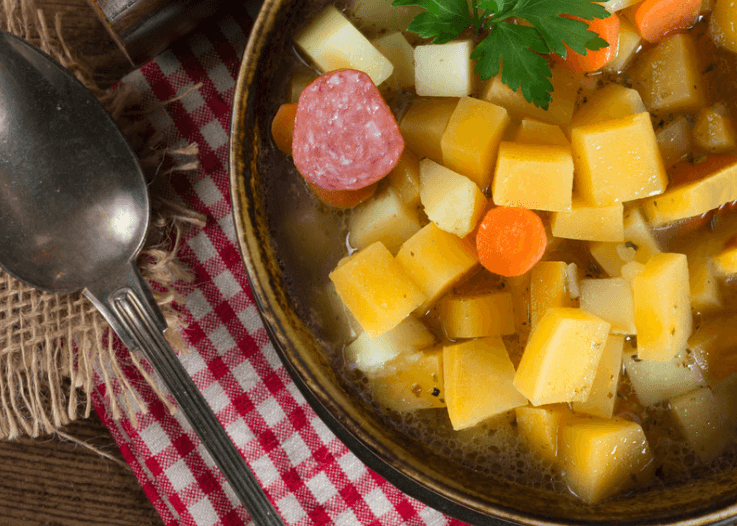 A closeup photo of a pot of rutabagas in a broth; the pot is sits next to a large spoon atop a red and white tea towel