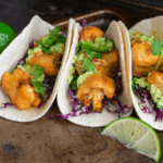 Three tacos with cauliflower with lime on the side.