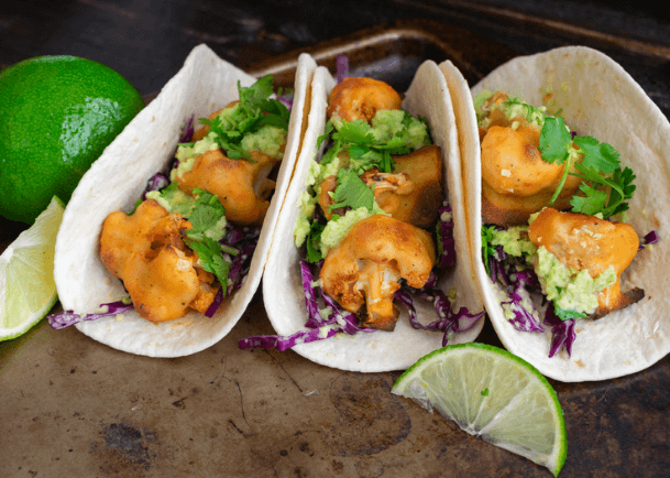 Three tacos with cauliflower with lime on the side.