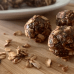 Cocoa nut butter balls on a wood cutting board with oats scattered around for garnish.