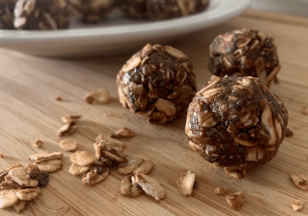 Cocoa nut butter balls on a wood cutting board with oats scattered around for garnish.